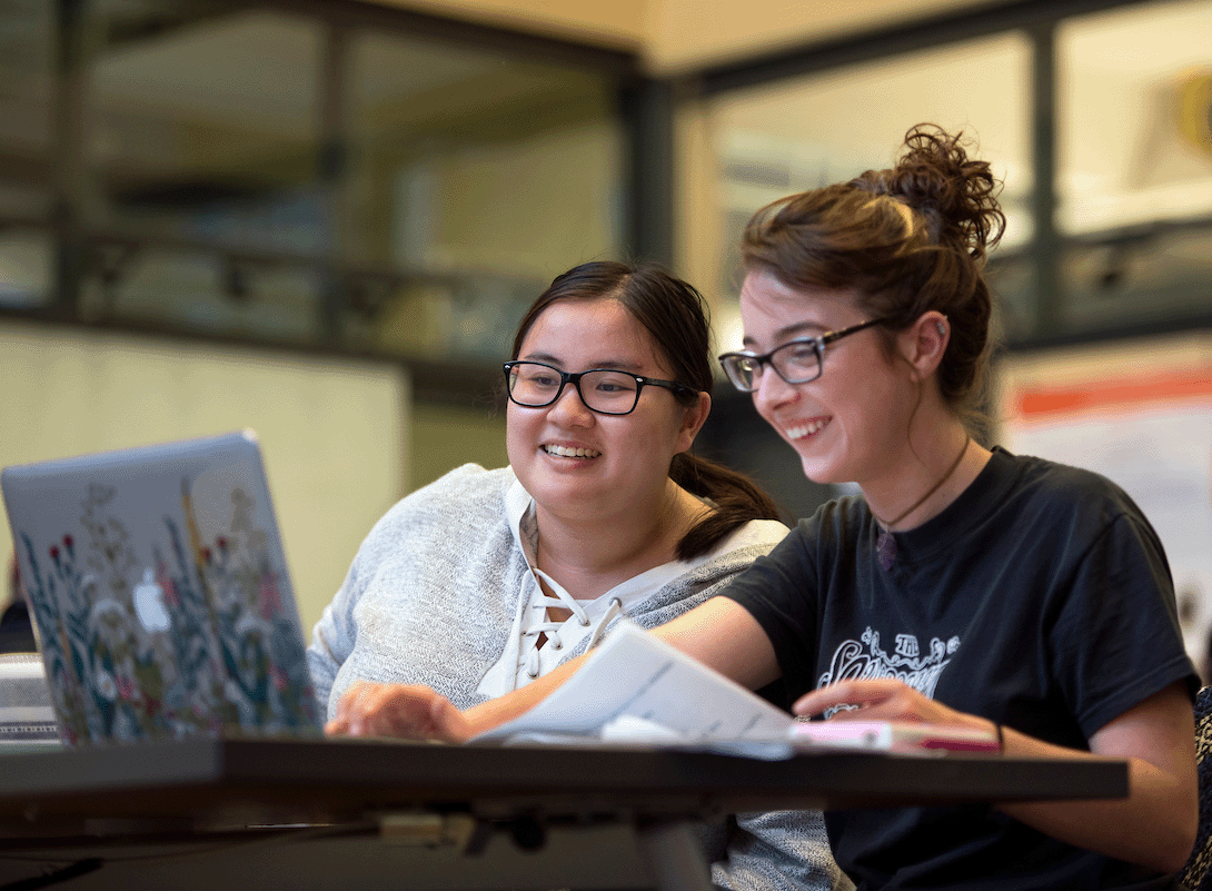 Two students enjoying a laugh together while viewing a laptop