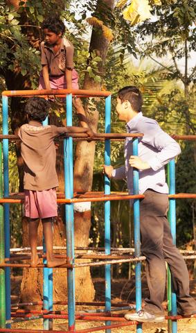 A student plays with some children on a playground in India